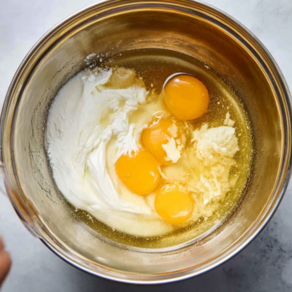 Easy Lemon Blueberry Bread Recipe 10 Top-down view of a stainless steel bowl containing eggs, butter, and a dollop of sour cream or yogurt, ready to be mixed together for a cake recipe.