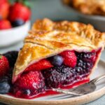 A freshly baked Mixed Berry Pie with a golden, flaky crust, filled with juicy strawberries, blueberries, and blackberries, served on a plate with a slice cut out to showcase the berry filling.
