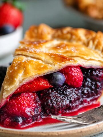 A freshly baked Mixed Berry Pie with a golden, flaky crust, filled with juicy strawberries, blueberries, and blackberries, served on a plate with a slice cut out to showcase the berry filling.