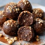 Chocolate hazelnut Nutella Protein Balls dusted with crushed nuts and cocoa powder, one cut in half showing the inside.