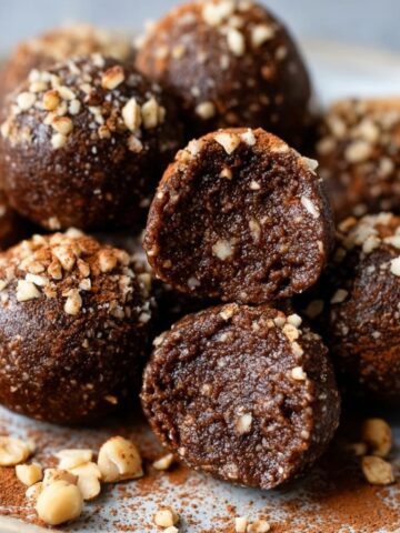 Easy Nutella Protein Balls Recipe 3 Chocolate hazelnut Nutella Protein Balls dusted with crushed nuts and cocoa powder, one cut in half showing the inside.