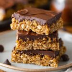 A close-up of Nutty Chocolate Bars with a thick layer of chocolate on top, stacked on a plate, showcasing their delicious, chewy texture.