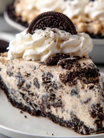 The Best Oreo Pie Recipe 2 A slice of Oreo pie with creamy filling, topped with whipped cream and a whole Oreo cookie, served on a white plate.