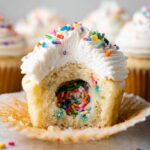 A Party Piñata Cupcakes with a white frosting topping, filled with colorful sprinkles inside.