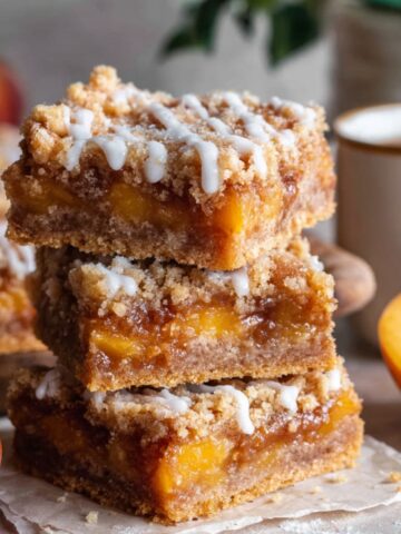 Easy Peach Cobbler Bars Recipe 2 A stack of freshly baked Peach Cobbler Bars with a golden crumble topping and sweet peach filling, drizzled with icing for extra sweetness.