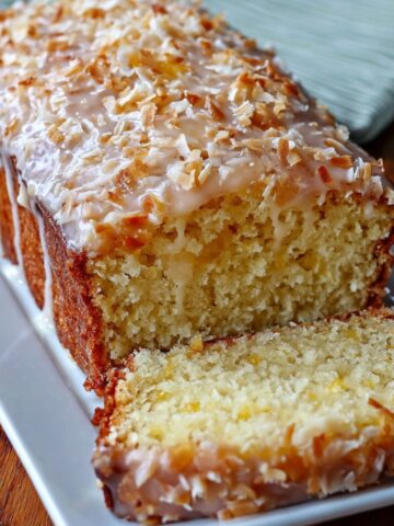 Easy Pineapple Coconut Bread Recipe 1 A close-up of a freshly baked loaf of Pineapple Coconut Bread with a glossy glaze and toasted coconut flakes on top. A slice has been cut, showing the soft interior.