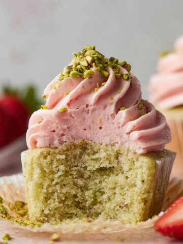 Pistachio Cupcakes topped with strawberry buttercream and pistachio bits.
