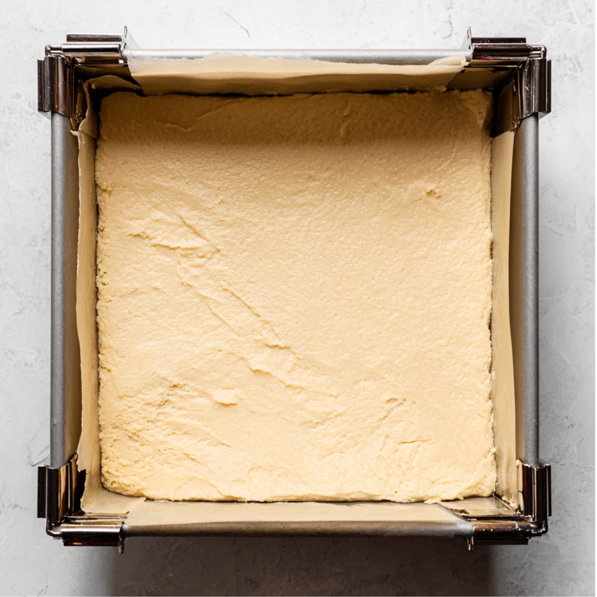 Easy Sugar Cookie Bars Recipe 11 A square baking pan filled with evenly pressed sugar cookie dough, ready to be baked.