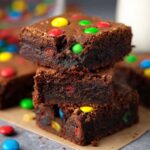 stack of fudgy Protein Brownies with M&Ms visible on top and inside. The brownies have a rich, dark chocolate texture, and the bright M&M's add a playful pop of color to the dessert.