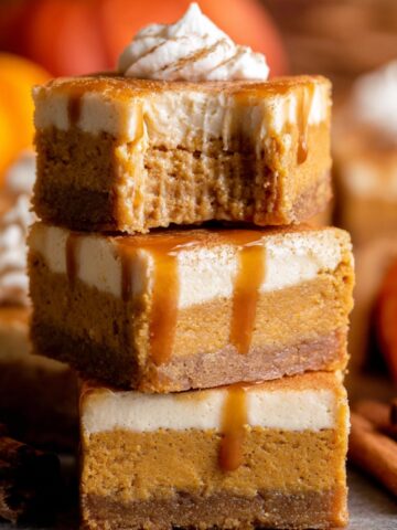 Pumpkin Cheesecake Bars Recipe 1 Stacked slices of Pumpkin Cheesecake Bars with a caramel drizzle and a dollop of whipped cream on top, showcasing their creamy texture.