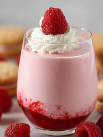 Easy Raspberry Mousse (Without Gelatin) 1 A glass filled with pink Raspberry Mousse, topped with a fresh raspberry and whipped cream. The mousse has a layer of raspberry coulis at the bottom, and is surrounded by fresh raspberries and cookies.