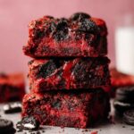 Stack of moist Red Velvet Oreo Brownies with visible Oreo chunks, dusted with powdered sugar, looking freshly baked and delicious.