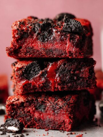 Easy Red Velvet Oreo Brownies Recipe 1 Stack of moist Red Velvet Oreo Brownies with visible Oreo chunks, dusted with powdered sugar, looking freshly baked and delicious.