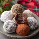 Plate of rum balls coated in sugar and cocoa, one cut in half.