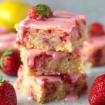 Stacked strawberry lemon blondies with a pink glaze on top, showing the soft, moist interior with chunks of strawberries and a glossy finish.