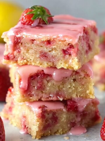 Stacked strawberry lemon blondies with a pink glaze on top, showing the soft, moist interior with chunks of strawberries and a glossy finish.
