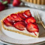 A beautifully sliced strawberry tart with fresh, juicy strawberries arranged on top of a creamy filling and crisp tart crust. The slice reveals the creamy interior and golden crust.