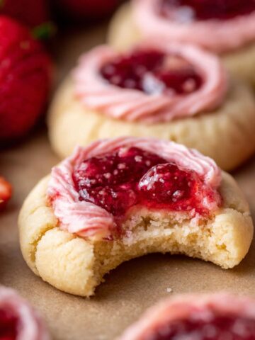 Bite taken from a Strawberry Thumbprint Cookies with pink cream and jam.