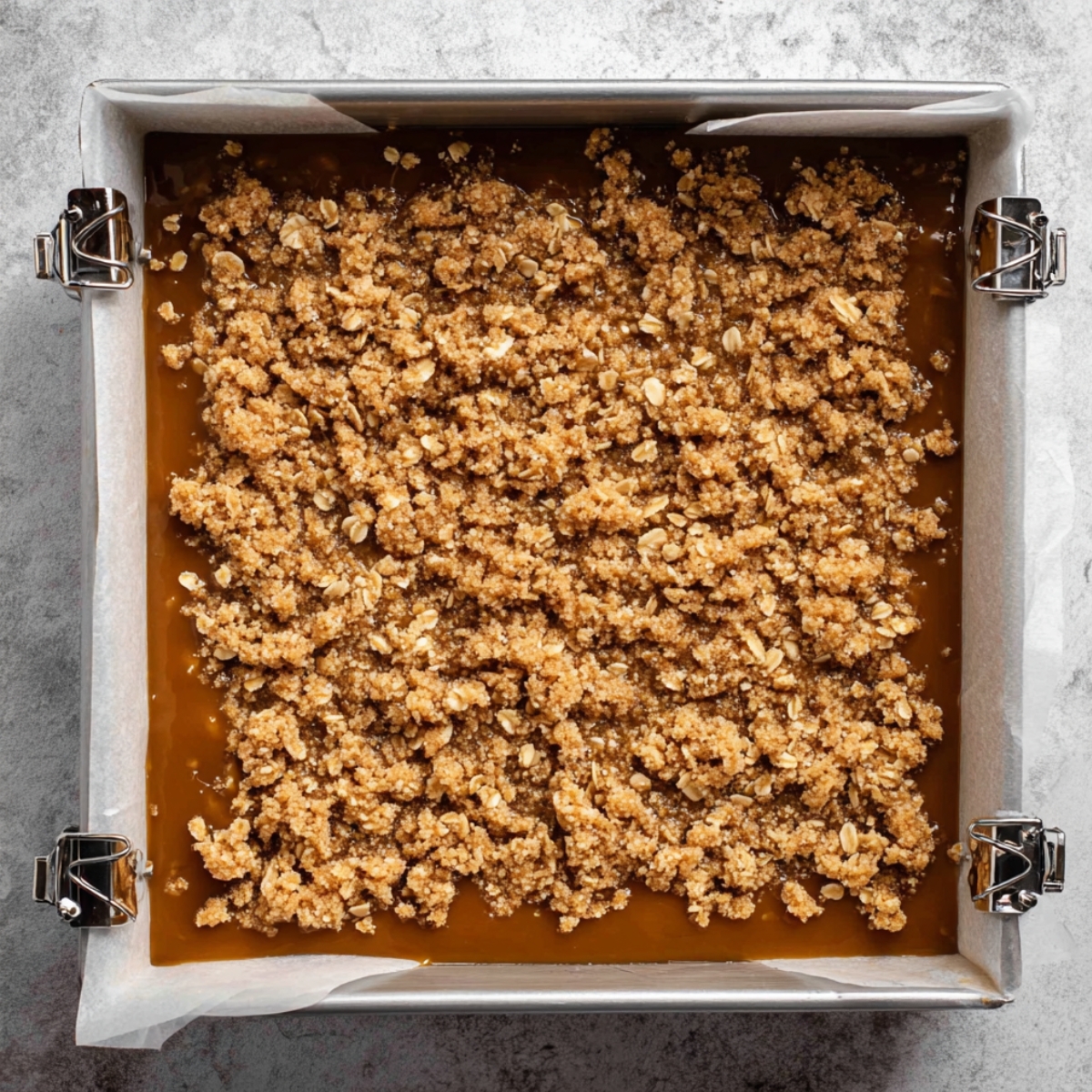 Carmelitas Recipe: Easy Caramel Chocolate Cookie Bars 11 A square baking pan filled with layers of caramel and a crumbly oat mixture, ready to be baked.
