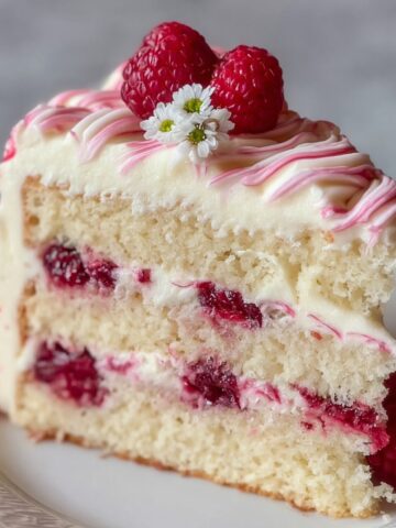 White Chocolate Raspberry Cake Recipe 1 A soft, moist slice of White Chocolate Raspberry Cake filled with raspberry jam, topped with fresh raspberries and white chocolate swirls.