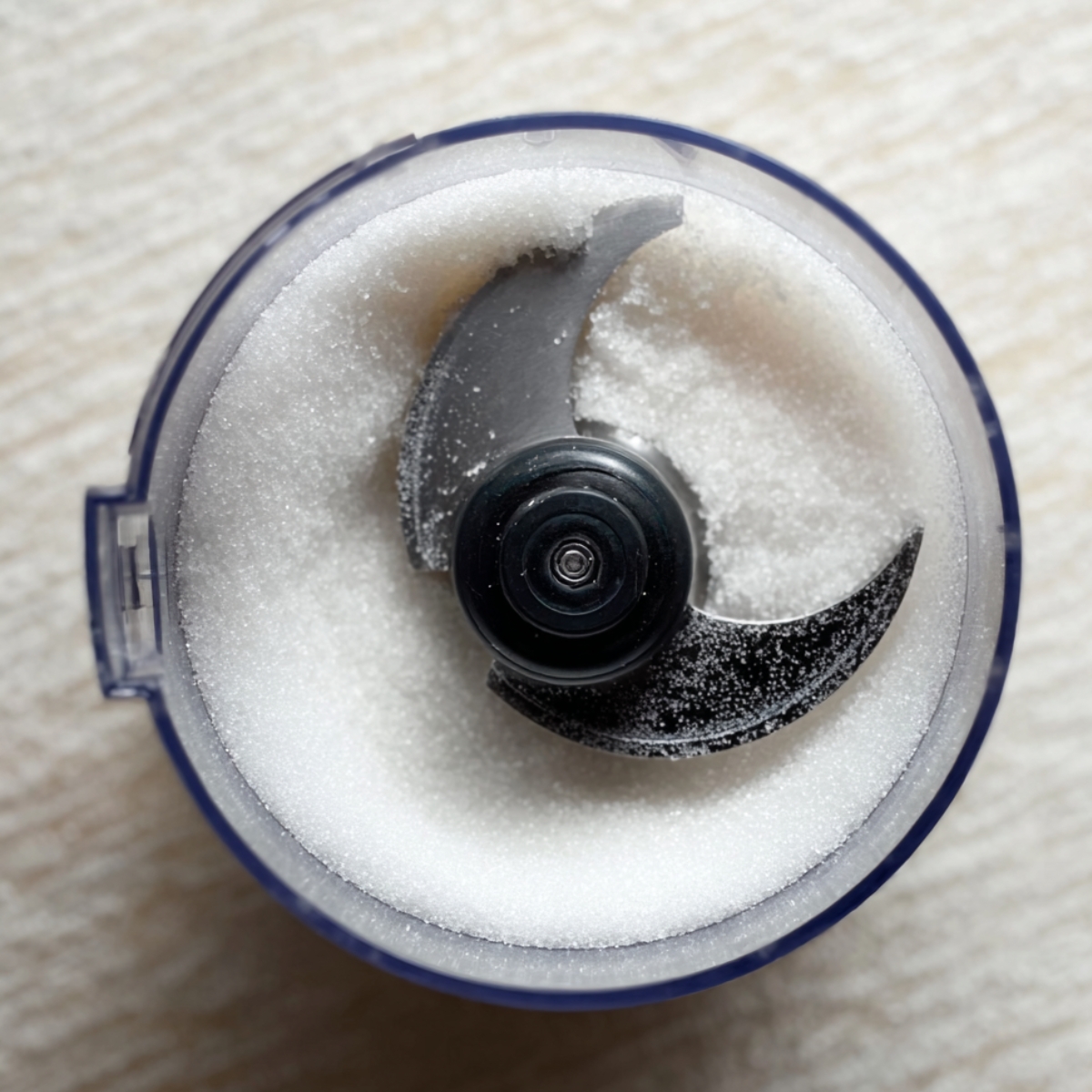 The Perfect Meringue Roulade Recipe 10 Close-up shot of a food processor with granulated sugar inside, before being pulsed to a fine consistency, with the blades visible.