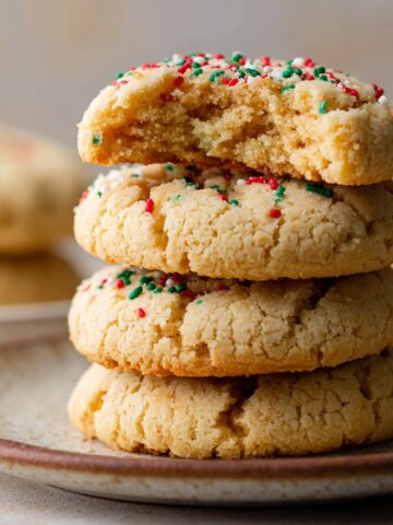 Easy Almond Flour Sugar Cookies Recipe 1 Stacked Almond Flour Sugar Cookies with festive red, green, and white sprinkles, top cookie partially bitten.