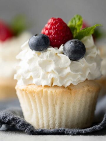 The Best Angel Food Cupcakes Recipe 1 Angel Food Cupcakes topped with fluffy whipped cream, fresh raspberries, blueberries, and mint leaves in elegant bakery-style photography.