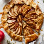 Rustic homemade Apple Galette with golden flaky crust, filled with thinly sliced cinnamon-spiced apples, drizzled with caramel sauce, with a slice partially lifted.
