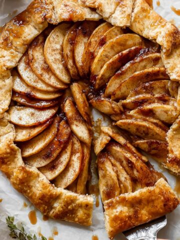 Easy Apple Galette Recipe 1 Rustic homemade Apple Galette with golden flaky crust, filled with thinly sliced cinnamon-spiced apples, drizzled with caramel sauce, with a slice partially lifted.