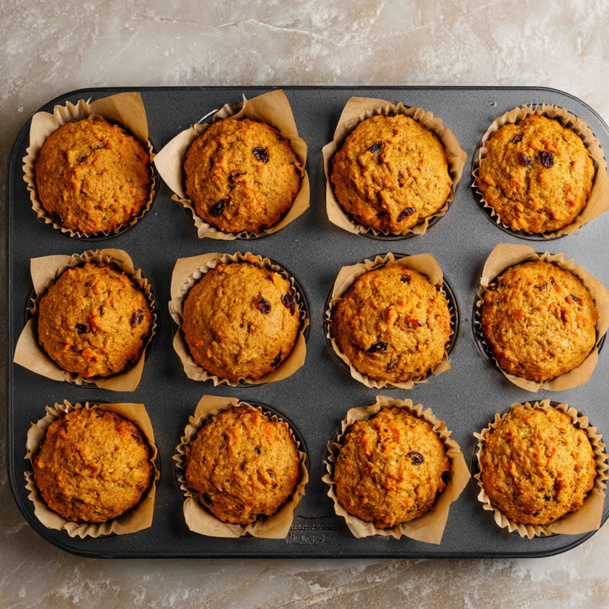 The Best Carrot Muffins Recipe 11 Stack of carrot muffins, one cut open, showing moist interior with carrots and nuts.