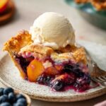 A freshly baked Blueberry Peach Pie with a golden lattice crust, filled with juicy fruit, and ready to be served. The crust is sprinkled with sugar for a sparkling finish.
