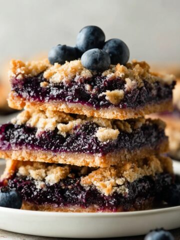 Easy Blueberry Pie Bars Recipe 1 Stack of homemade Blueberry Pie Bars with buttery crumble topping and fresh blueberries on a white plate, rustic bakery-style dessert photography.
