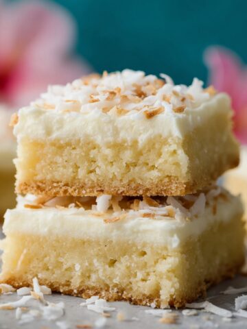 Easy Coconut Cream Bars Recipe 2 Two stacked Coconut Cream Bars dessert bars with creamy frosting and toasted coconut flakes on top, set on a light surface with soft pastel background for a bright, inviting look.