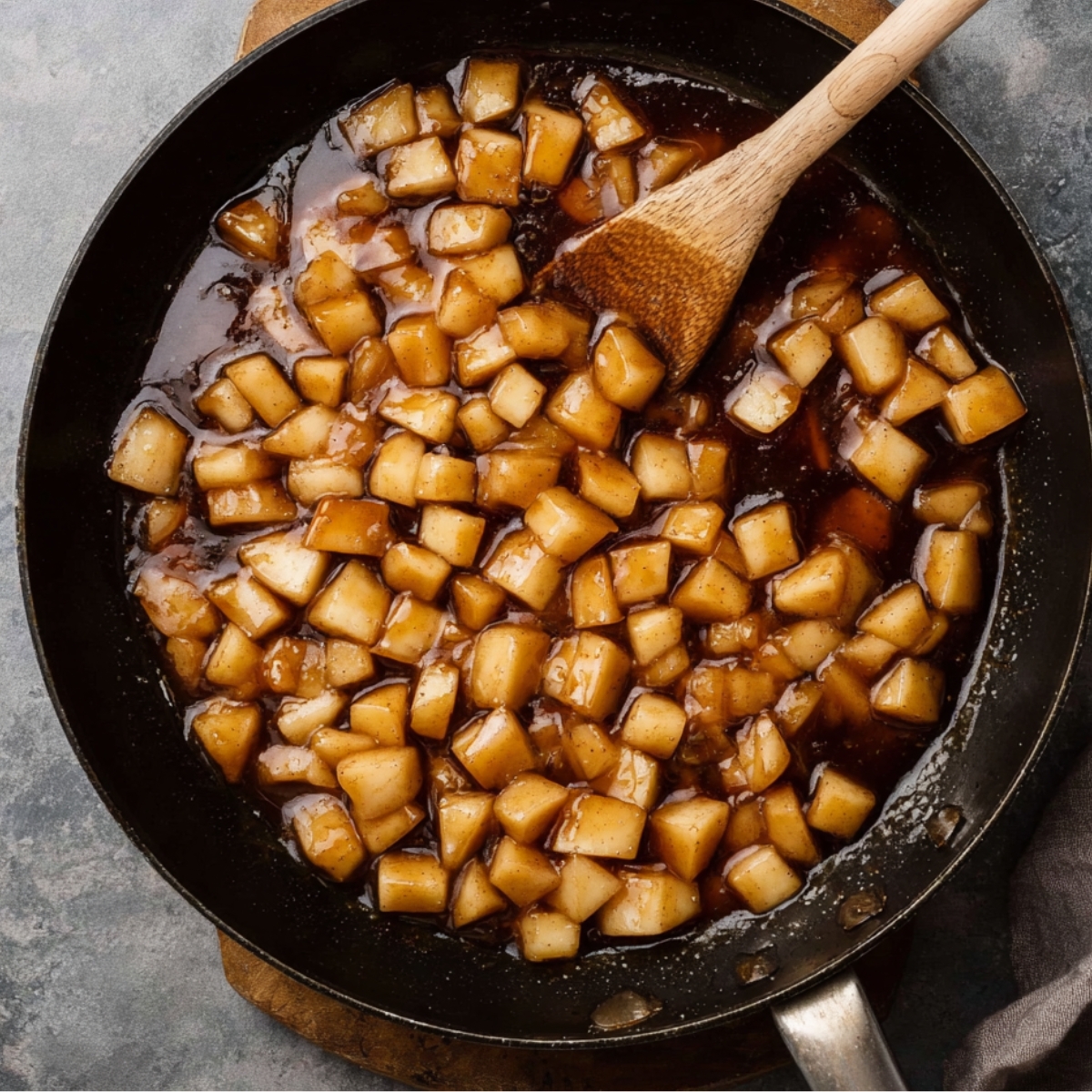 Easy Apple Fritter Cake Recipe 10 Diced apples cooking in a skillet with syrup and a wooden spoon.