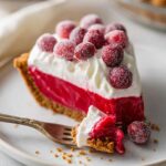 Slice of Cranberry Curd Tart with graham cracker crust, topped with whipped cream and sugared cranberries on a white plate with a fork.