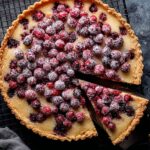 Unbaked cranberry frangipane tart with fresh cranberries arranged over almond filling in a crumb crust tart shell.