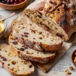 Sliced Cranberry Nut No-Knead Bread with a soft, airy interior, served with butter.