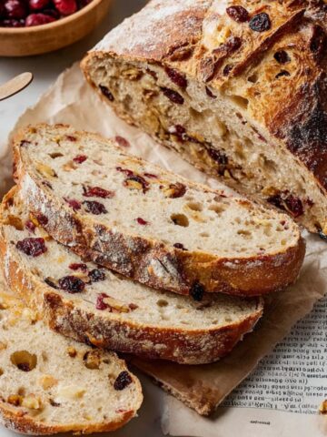 Sliced Cranberry Nut No-Knead Bread with a soft, airy interior, served with butter.