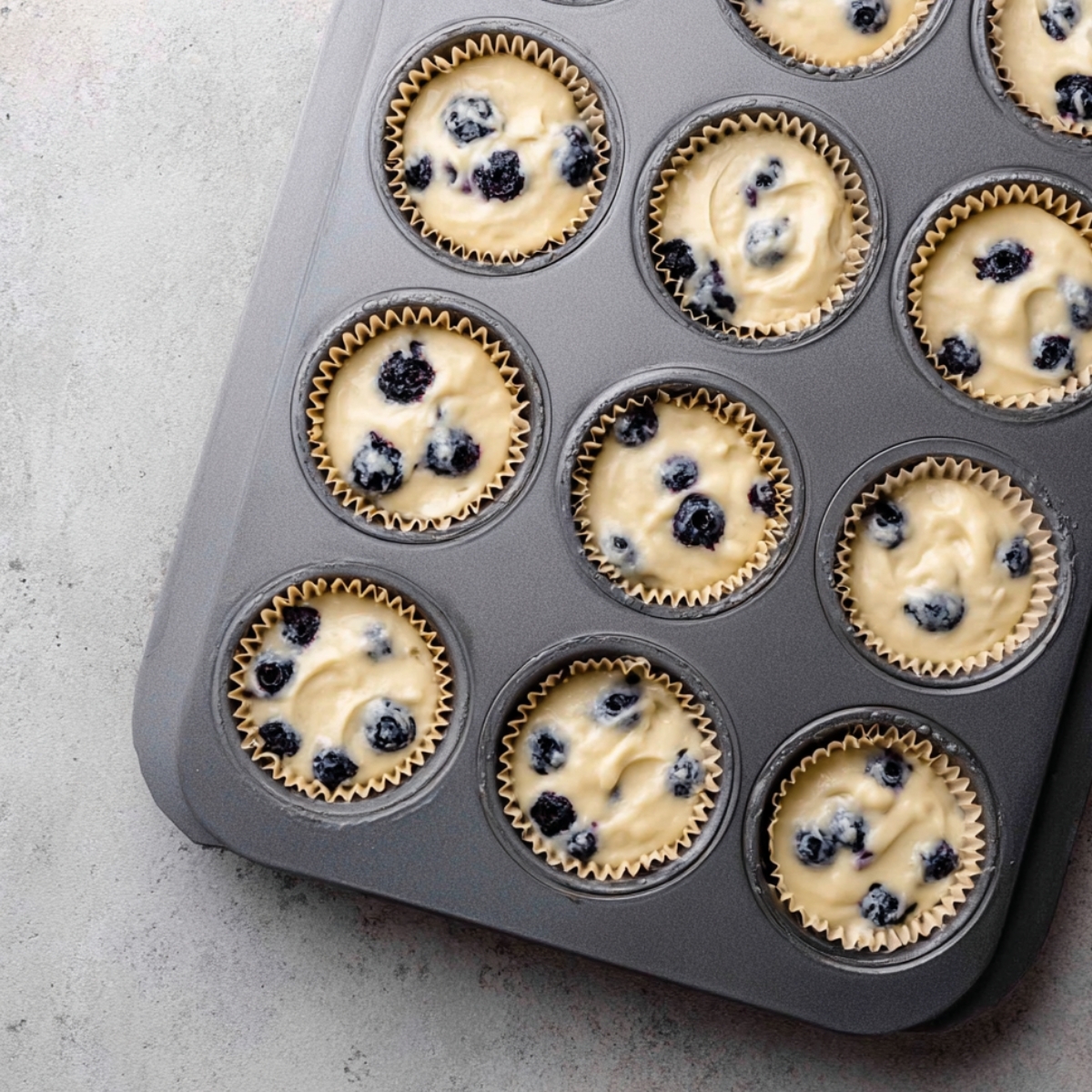Blueberry Cream Cupcakes Recipe 11 Blueberry cupcake batter in paper liners in a muffin tray.