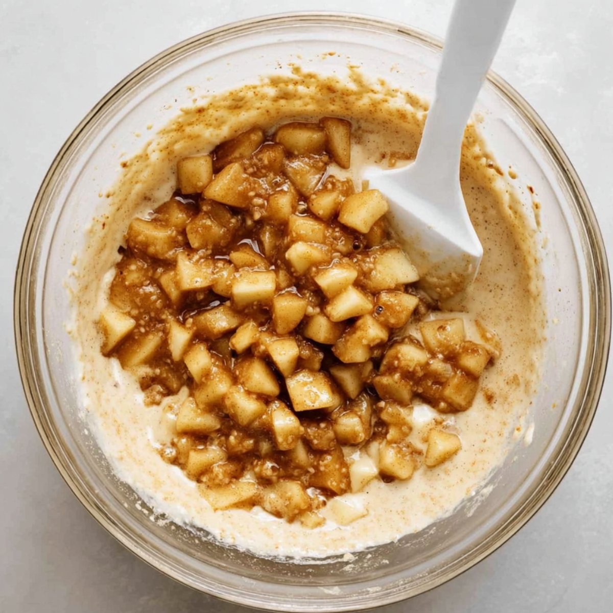Easy Apple Fritter Cake Recipe 11 Apple pieces folded into cake batter in a mixing bowl with a spatula.