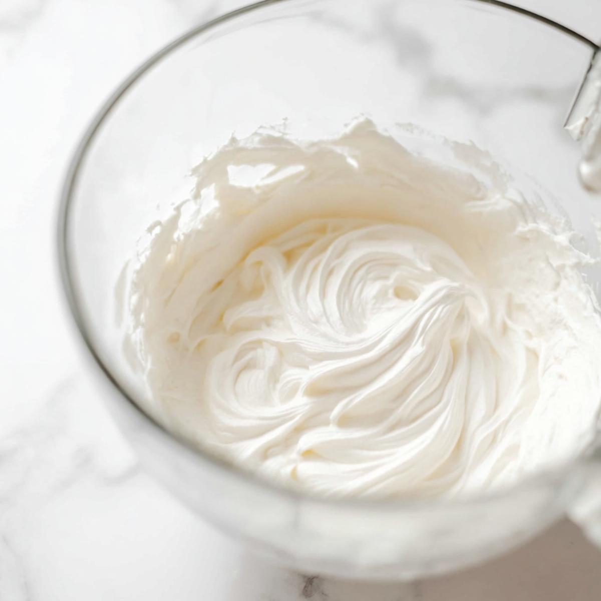 Easy No Bake Cheesecake Jars Recipe 11 Smooth creamy cheesecake filling swirled inside a clear glass mixing bowl on a white marble countertop.