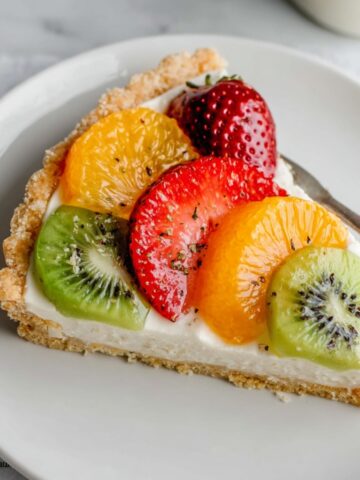 A slice of Fresh Fruit Tart topped with vibrant strawberries, oranges, and kiwi on a smooth, creamy filling with a crumbly tart crust.