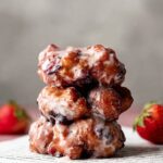 Fried Berry Fritters with a glossy glaze, stacked on top of each other with a strawberry on the side.