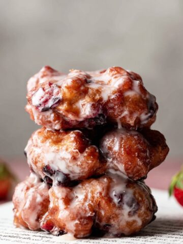 Fried Berry Fritters with a glossy glaze, stacked on top of each other with a strawberry on the side.