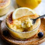 Baked Lemon Pudding Cakes in a ramekin with lemon slice and blueberries, spoon scooping.