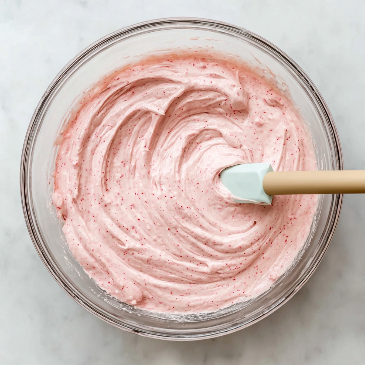 Raspberry Cheesecake Brownies Recipe 10 Creamy pink raspberry cheesecake batter swirled smoothly in a clear glass mixing bowl with a silicone spatula.
