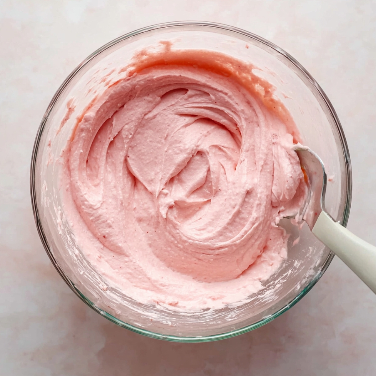 Easy Strawberry Cake Roll Recipe 11 Glass mixing bowl with smooth cream cheese base for strawberry cake roll, wooden spatula inside.
