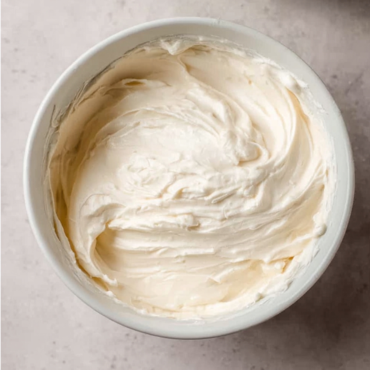 Easy Oatmeal Cream Pie Cake Recipe 11 A white bowl filled with smooth, creamy frosting, with a spoon resting on the side, ready to be spread on a cake.