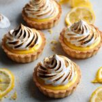 Mini Lemon Meringue Tarts with golden, toasted meringue swirls on top, showcasing the bright yellow lemon curd filling inside a golden tart shell.