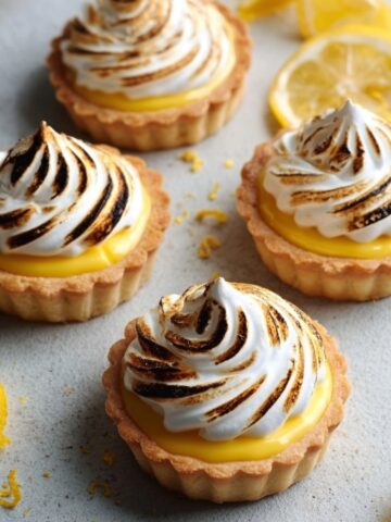 Easy Mini Lemon Meringue Tarts 2 Mini Lemon Meringue Tarts with golden, toasted meringue swirls on top, showcasing the bright yellow lemon curd filling inside a golden tart shell.